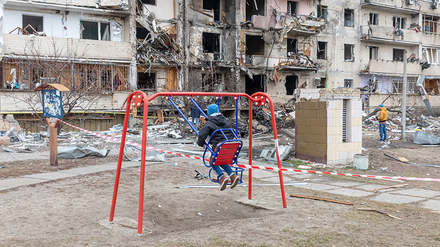 A child on a swing in front of a residential building damaged by a rocket in Kyiv, Ukraine. February 2022